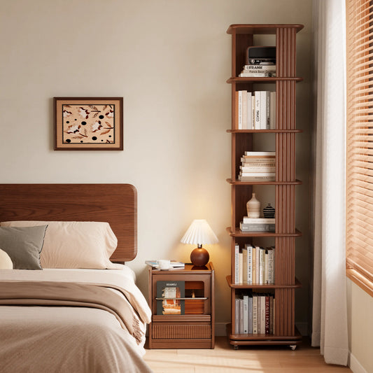 Tall rotating bookshelf filled with books beside a bed