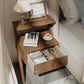Wooden nightstand with open drawer, books, a cup, and a lamp in a bedroom setting.