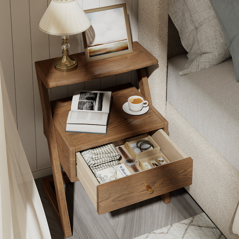 Wooden nightstand with open drawer, books, a cup, and a lamp in a bedroom setting.